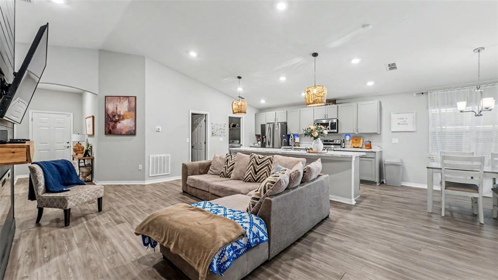 An open-concept living room and kitchen feature gray cabinetry, wood-look flooring, and a sectional sofa — 1244 MEZZAVALLE WAY, AUBURNDALE, FL