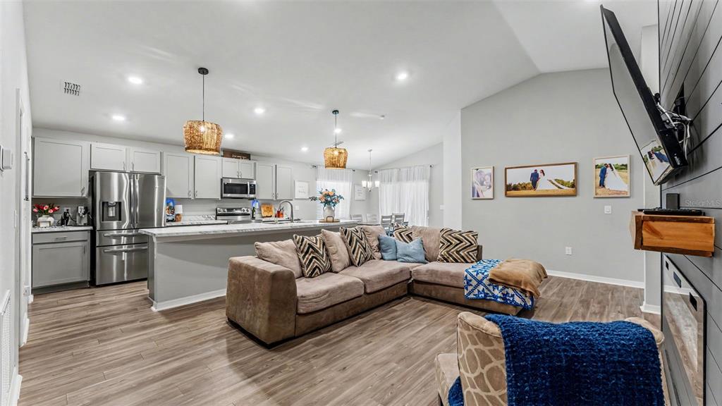 An open-concept living room and kitchen featuring light gray cabinetry, stainless appliances, and wood flooring — 1244 MEZZAVALLE WAY, AUBURNDALE, FL