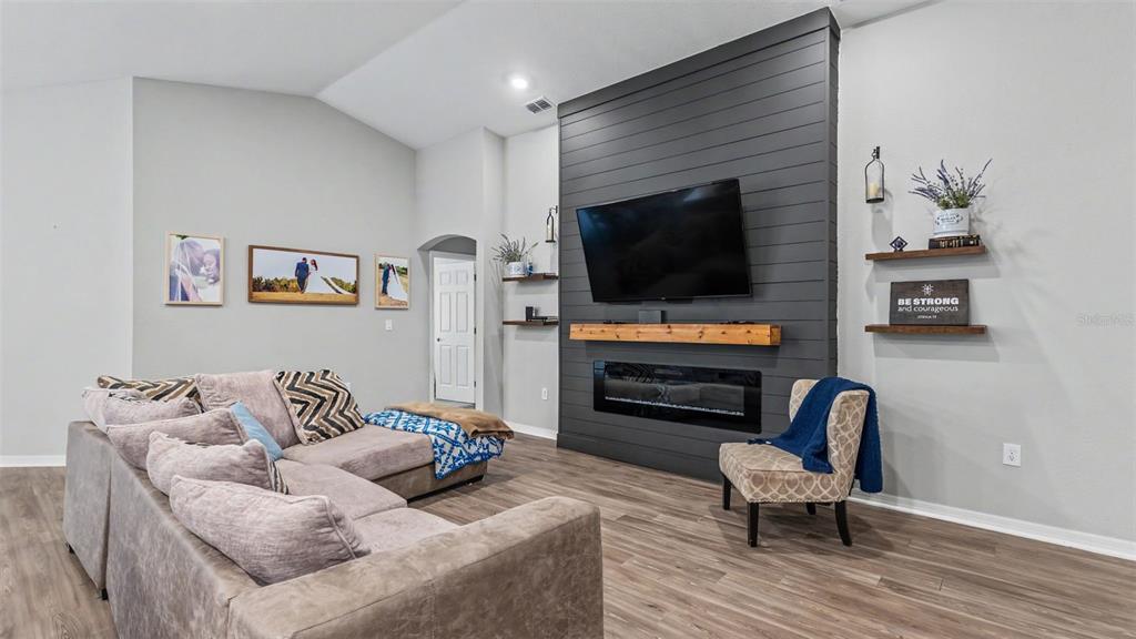 A living room features a gray shiplap fireplace wall, a sectional sofa, and wood flooring — 1244 MEZZAVALLE WAY, AUBURNDALE, FL