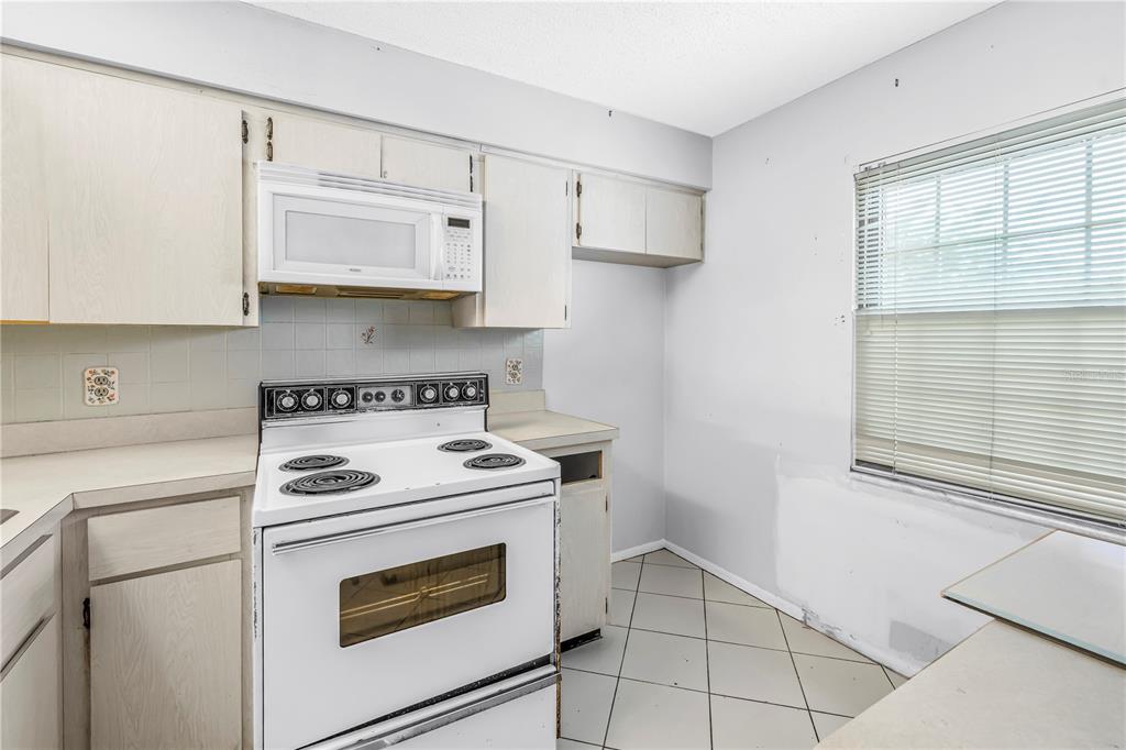 A kitchen features white cabinets, a white stove, a microwave, and light-colored tile flooring — 4774 LAKE BOULEVARD UNIT 9B, CLEARWATER, FL