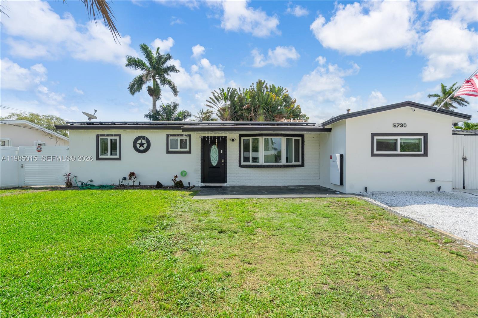 A single-story white house with a dark trim, a front lawn, and a Tesla Powerwall — 5730 SW 55th St, Davie FL 33314, DAVIE, FL