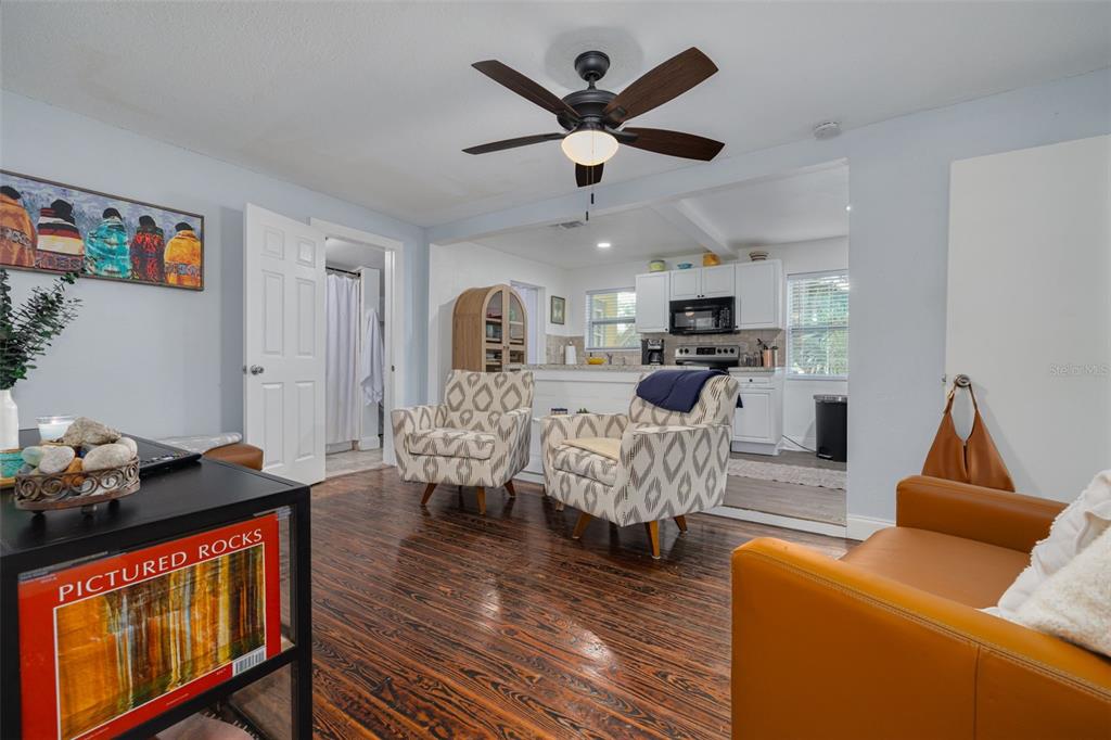 A living room with dark wood floors, two patterned armchairs, and an open kitchen beyond — 5721 CASSON AVENUE, NEW PORT RICHEY, FL