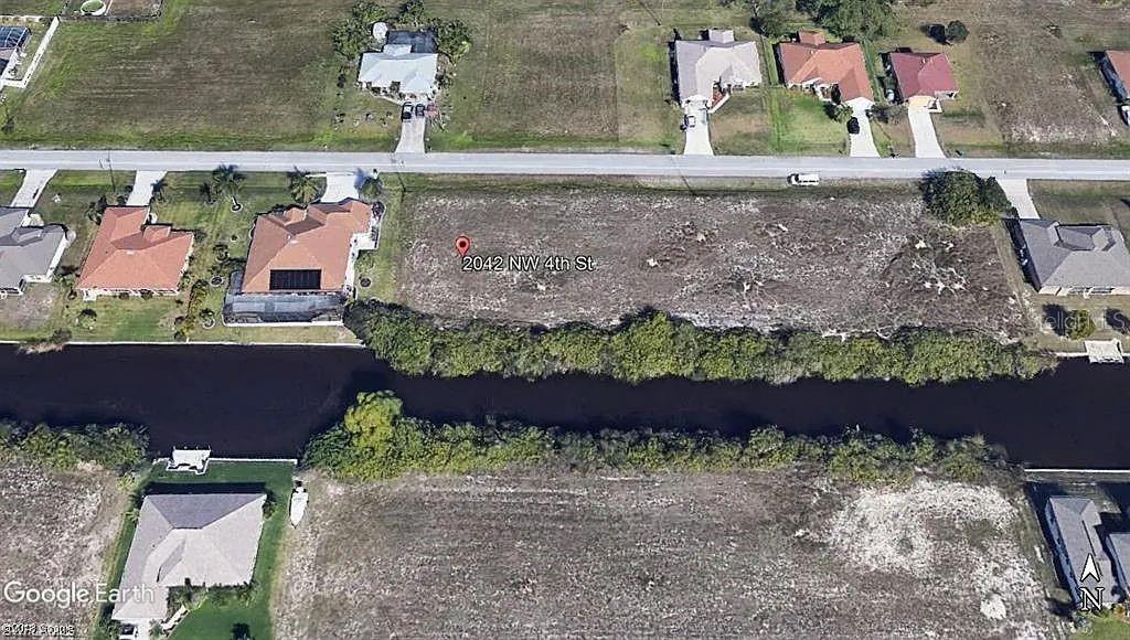 This aerial view shows a vacant residential lot situated between two houses along a canal — 2042 NW 4TH STREET, CAPE CORAL, FL