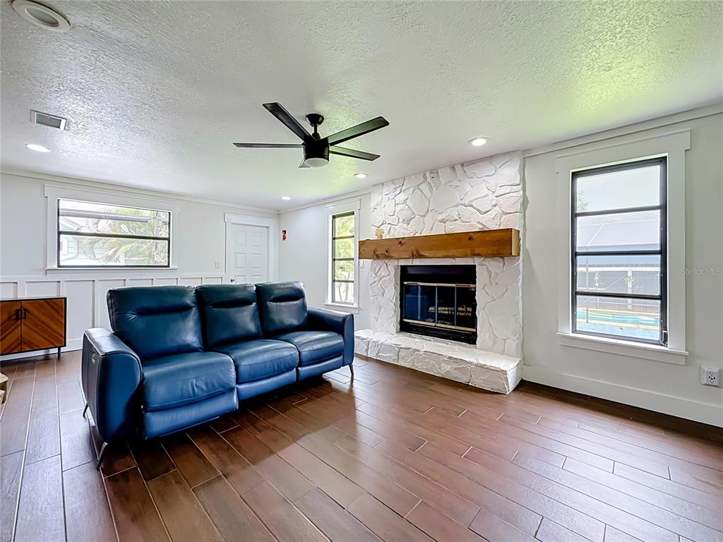 A living room features a blue leather sofa, a white stone fireplace, and wood flooring — 12756 POINSETTIA AVENUE, SEMINOLE, FL