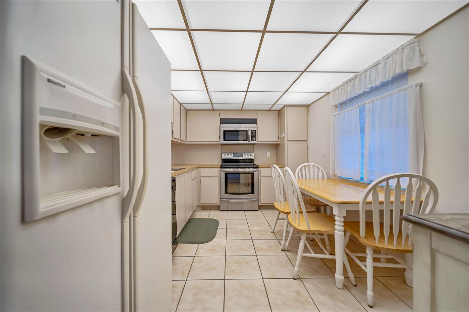 A kitchen with white cabinets, stainless steel appliances, a dining table, and a grid ceiling — 801 Cypress Boulevard # 107c, Pompano Beach FL 33069, POMPANO BEACH, FL
