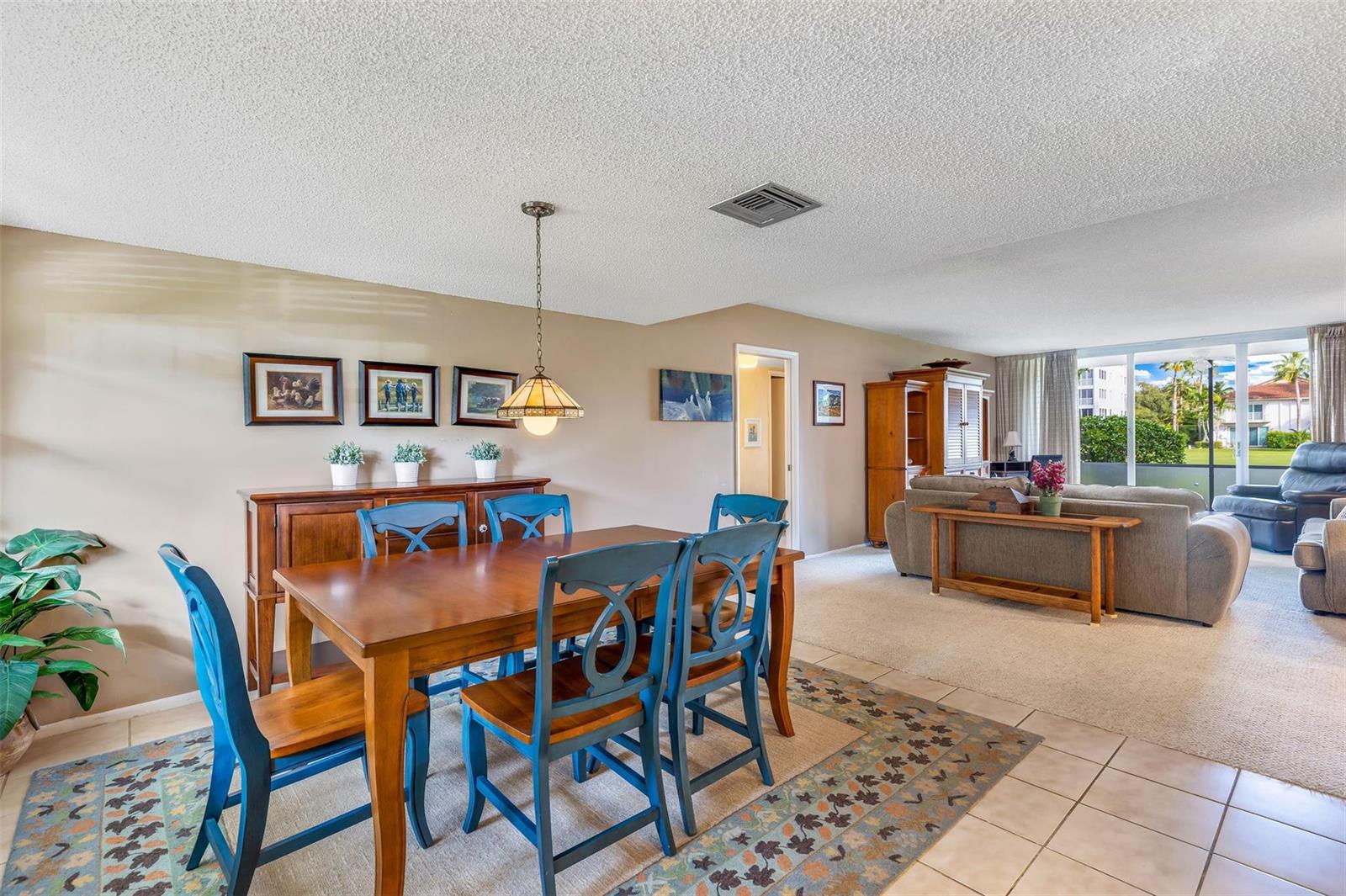 A dining area with a wooden table and blue chairs sits adjacent to a living room — 801 Cypress Boulevard # 107c, Pompano Beach FL 33069, POMPANO BEACH, FL