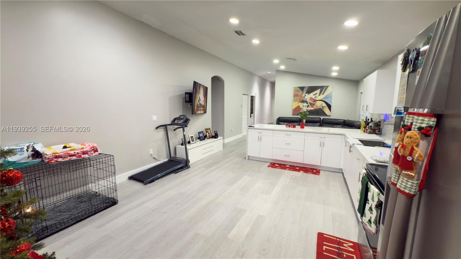 This open-concept kitchen and living area features white cabinetry, light wood-look flooring, and a treadmill — 2006 SE 14th Ct # 0, Homestead FL 33035, HOMESTEAD, FL