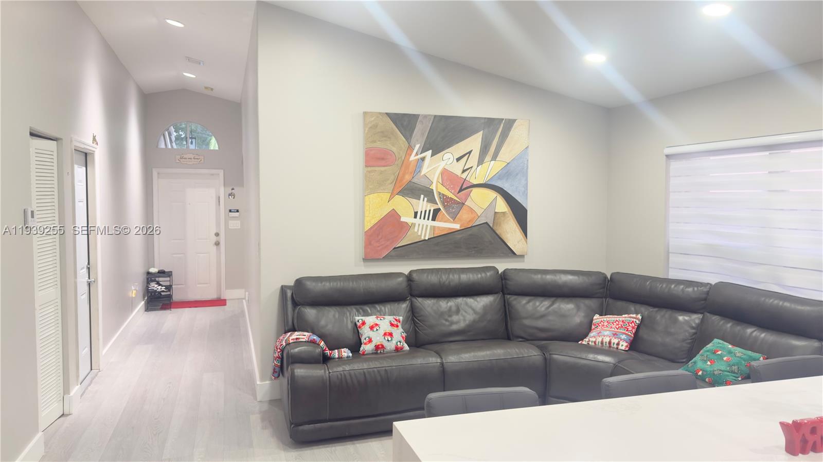 A living room features a dark leather sectional sofa, abstract wall art, and light flooring — 2006 SE 14th Ct # 0, Homestead FL 33035, HOMESTEAD, FL