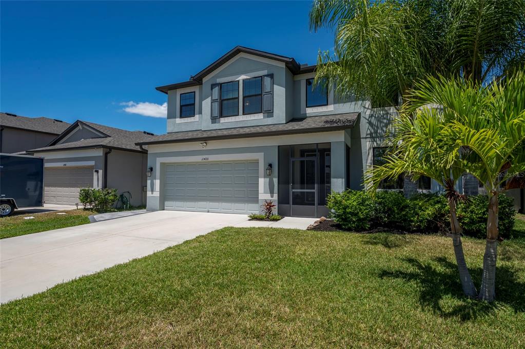 A two-story suburban house with a light blue exterior, a two-car garage, and a palm tree — 11420 AMAPOLA BLOOM COURT, RIVERVIEW, FL