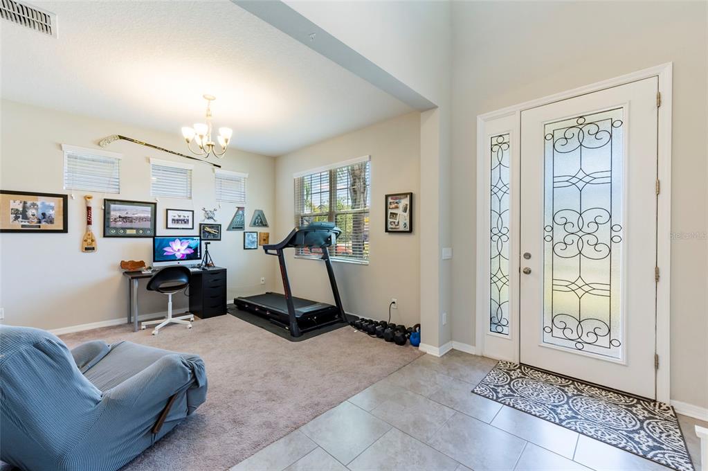 A room with carpeted flooring features a desk, a treadmill, and a front entry door — 11420 AMAPOLA BLOOM COURT, RIVERVIEW, FL