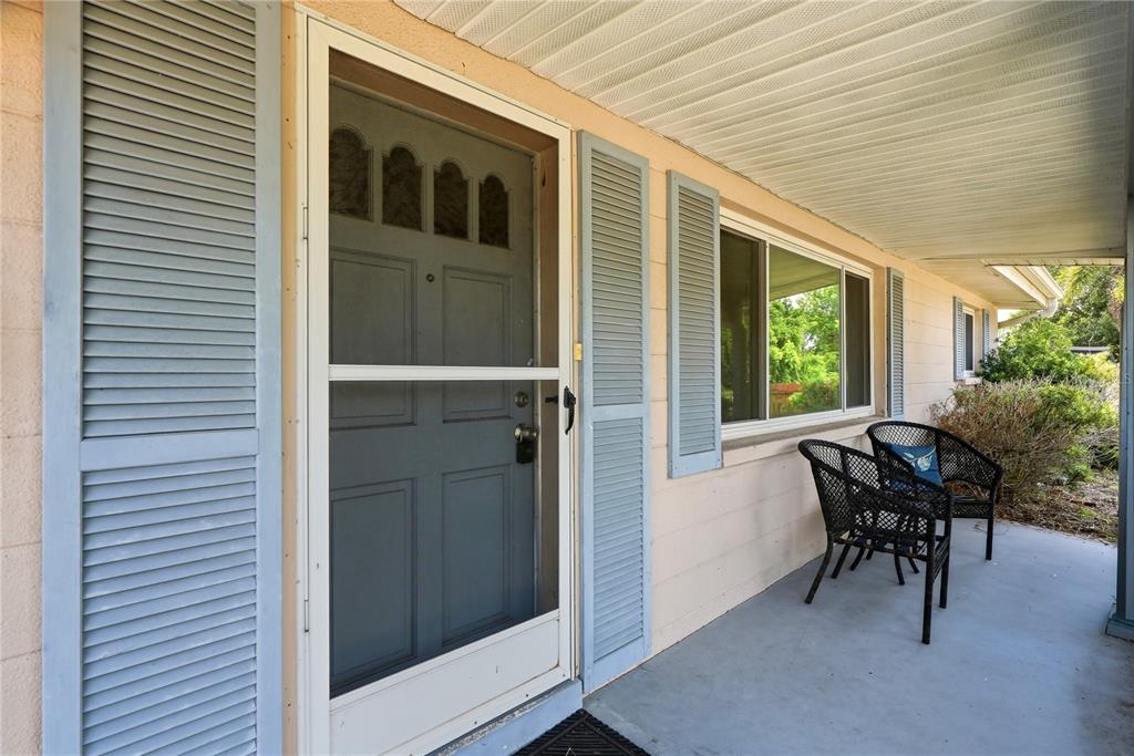A covered porch features a gray front door, blue shutters, and two black wicker chairs — 5123 20TH STREET W, BRADENTON, FL