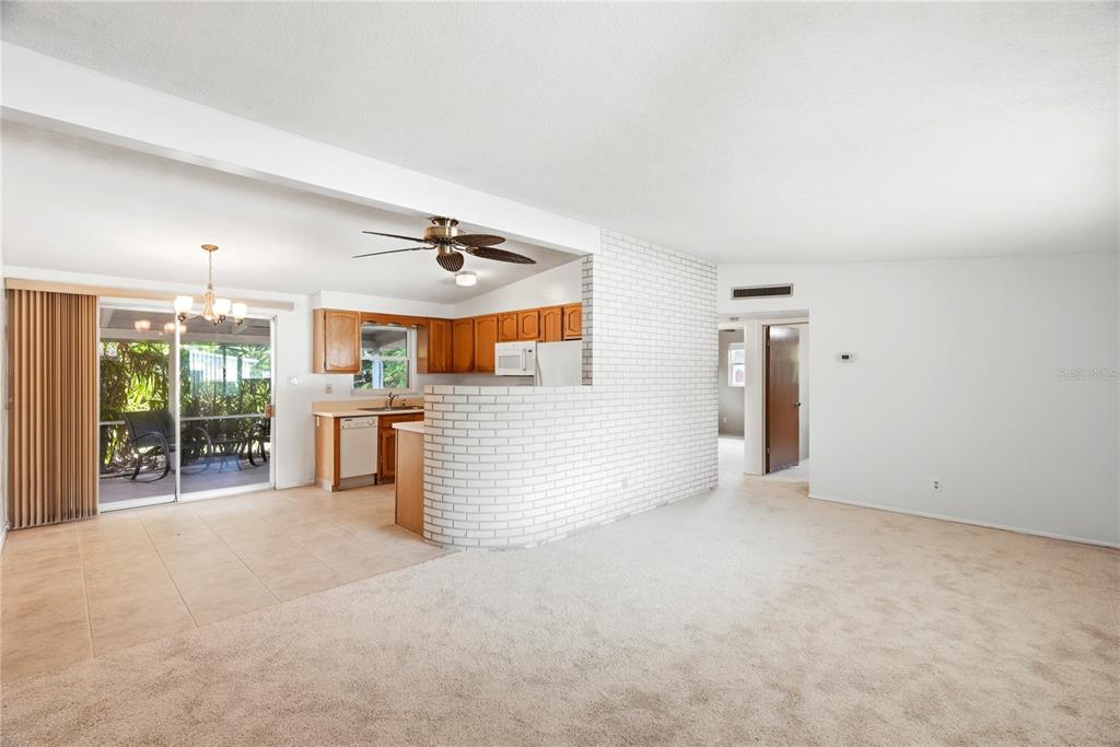 A living room with beige carpet leads to a kitchen featuring a white brick peninsula — 5123 20TH STREET W, BRADENTON, FL