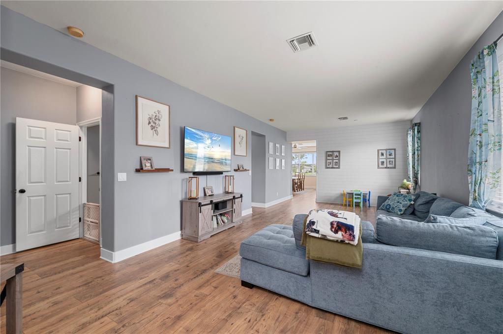 A living room features gray walls, wood-look flooring, a blue sectional sofa, and a television — 25538 PRADA DRIVE, PUNTA GORDA, FL