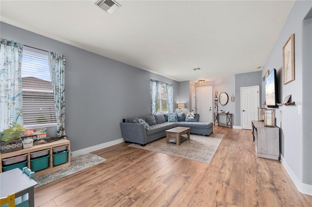 A living room with gray walls, wood-look flooring, a sectional sofa, and a television — 25538 PRADA DRIVE, PUNTA GORDA, FL