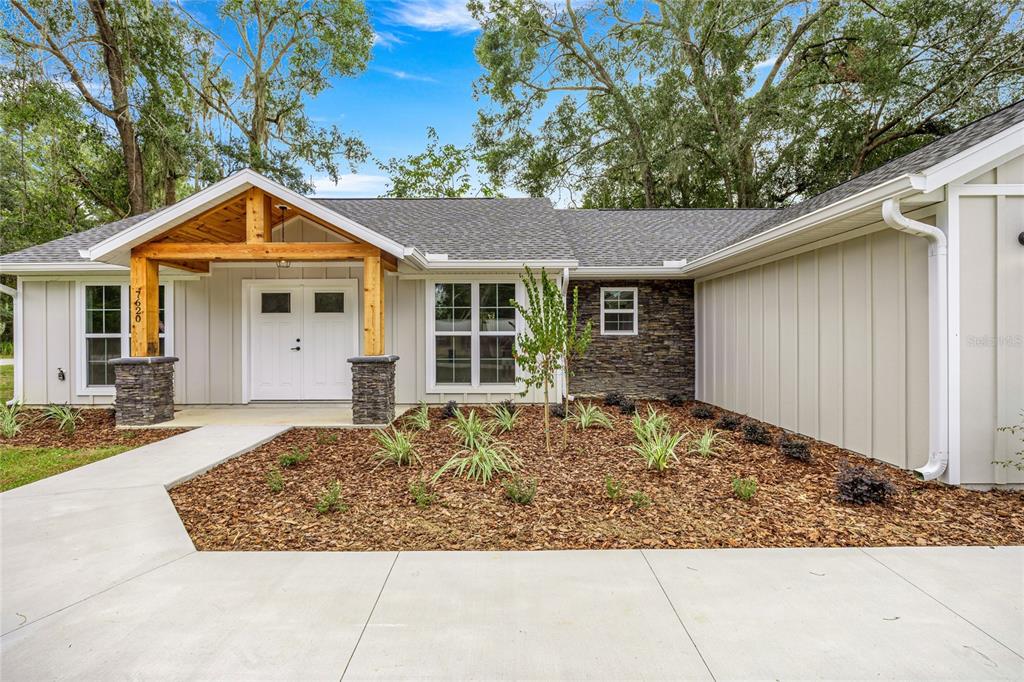 A single-story house exterior features a covered porch with stone pillars and light-colored siding — 7620 SW 78TH PLACE, OCALA, FL