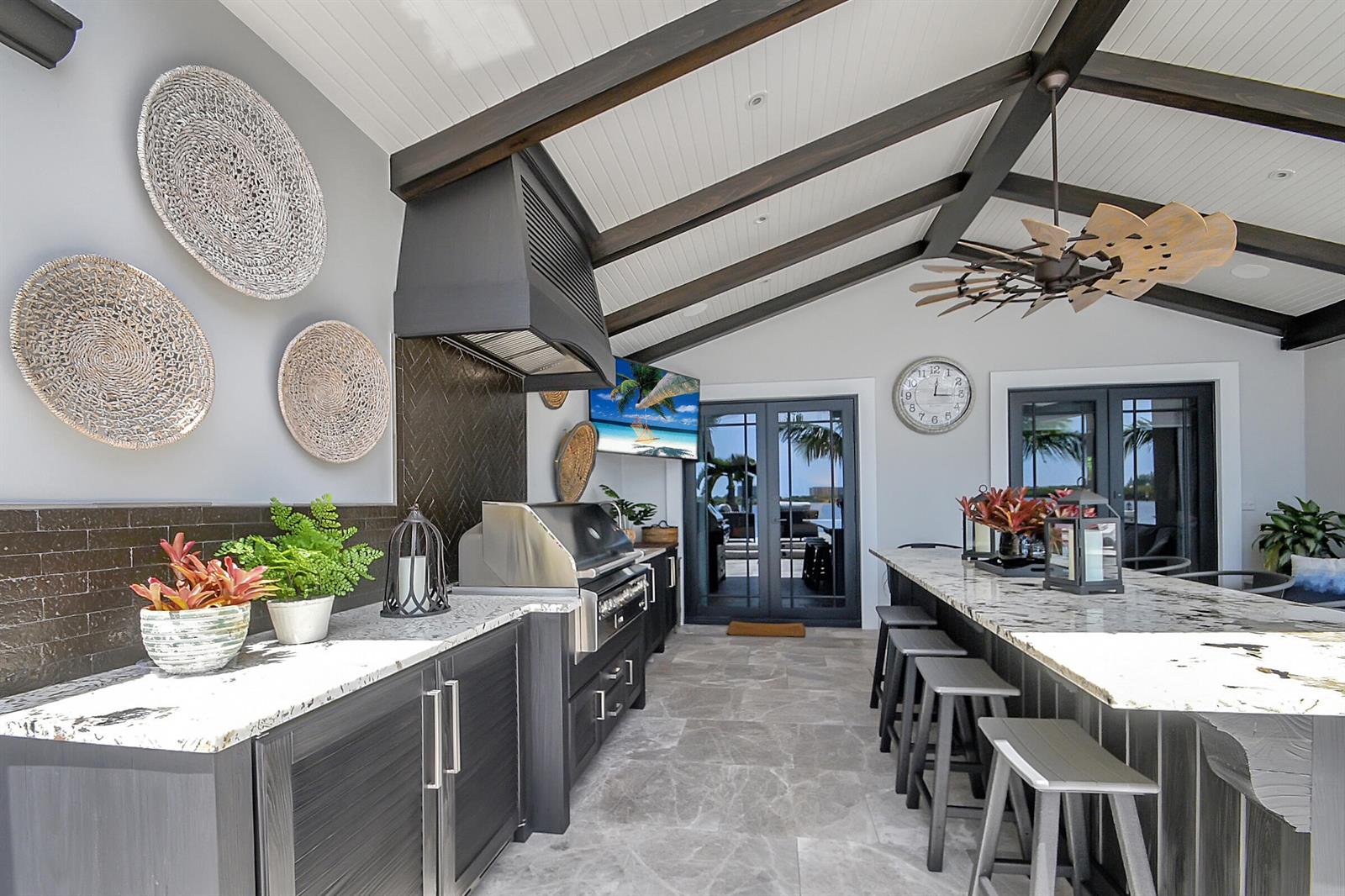 This outdoor kitchen features dark cabinetry, a stone countertop, a grill, and a vaulted ceiling — 1 Duke Drive, FL 33460, FL