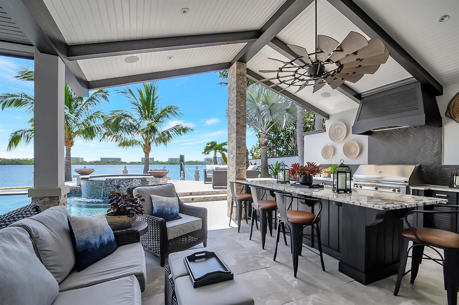 An outdoor covered patio features a kitchen island, bar seating, and a view of a pool — 1 Duke Drive, FL 33460, FL