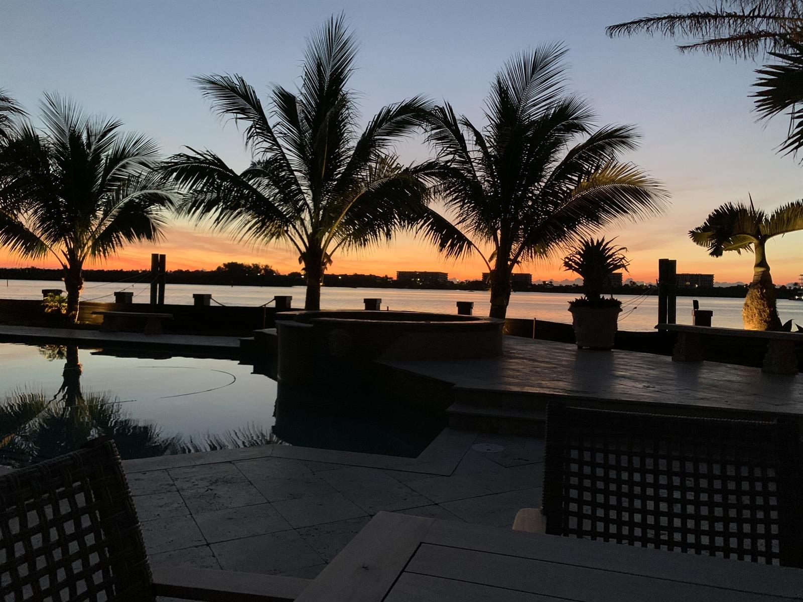 A swimming pool and hot tub overlook a waterfront sunset with silhouetted palm trees — 1 Duke Drive, FL 33460, FL