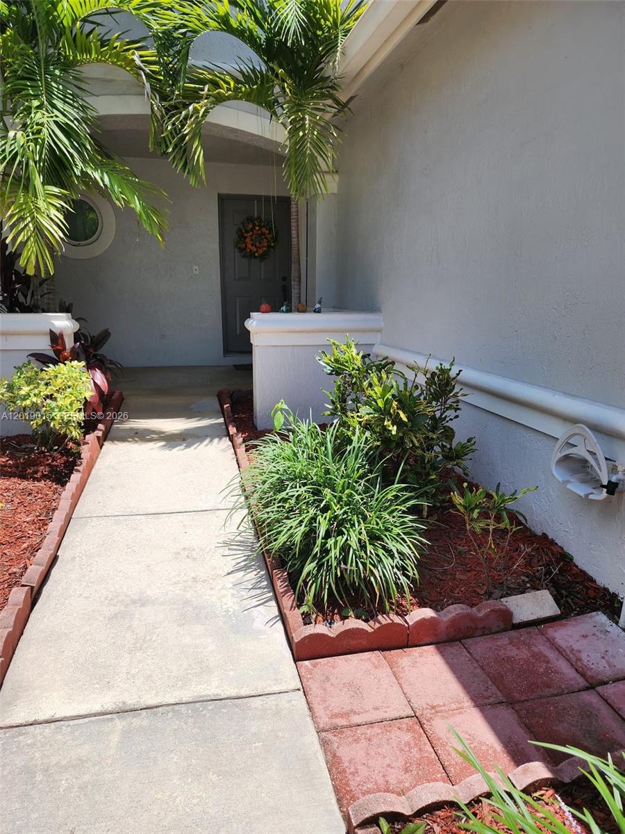 A concrete walkway leads to a front entrance with landscaping and a palm tree — 8014 Big Pine Way, Riviera Beach FL 33407, RIVIERA BEACH, FL