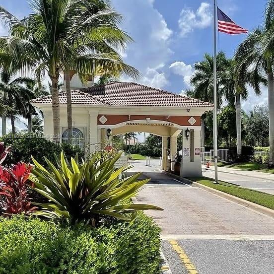 A gated community entrance features a beige guardhouse with a tiled roof and palm trees — 8014 Big Pine Way, Riviera Beach FL 33407, RIVIERA BEACH, FL