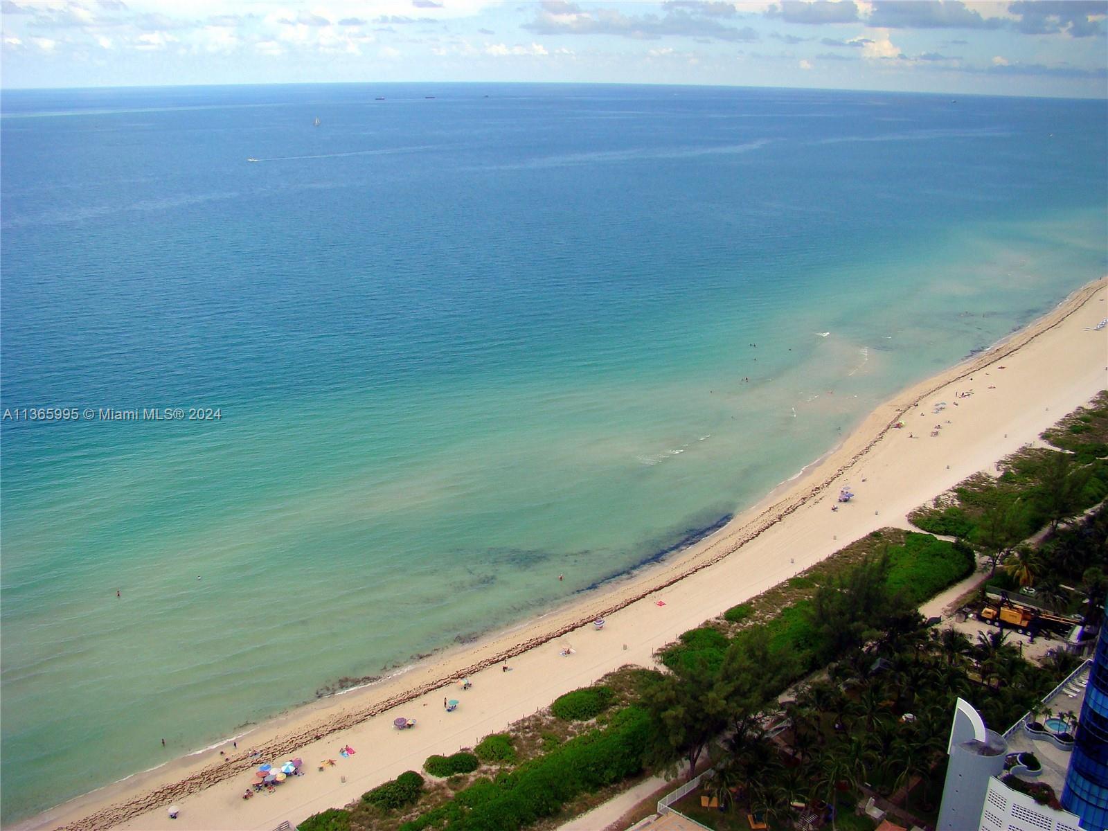 An aerial view shows a sandy beach along the ocean with lush green vegetation nearby — 6365 COLLINS AV # 3407, Miami Beach FL 33141, MIAMI BEACH, FL