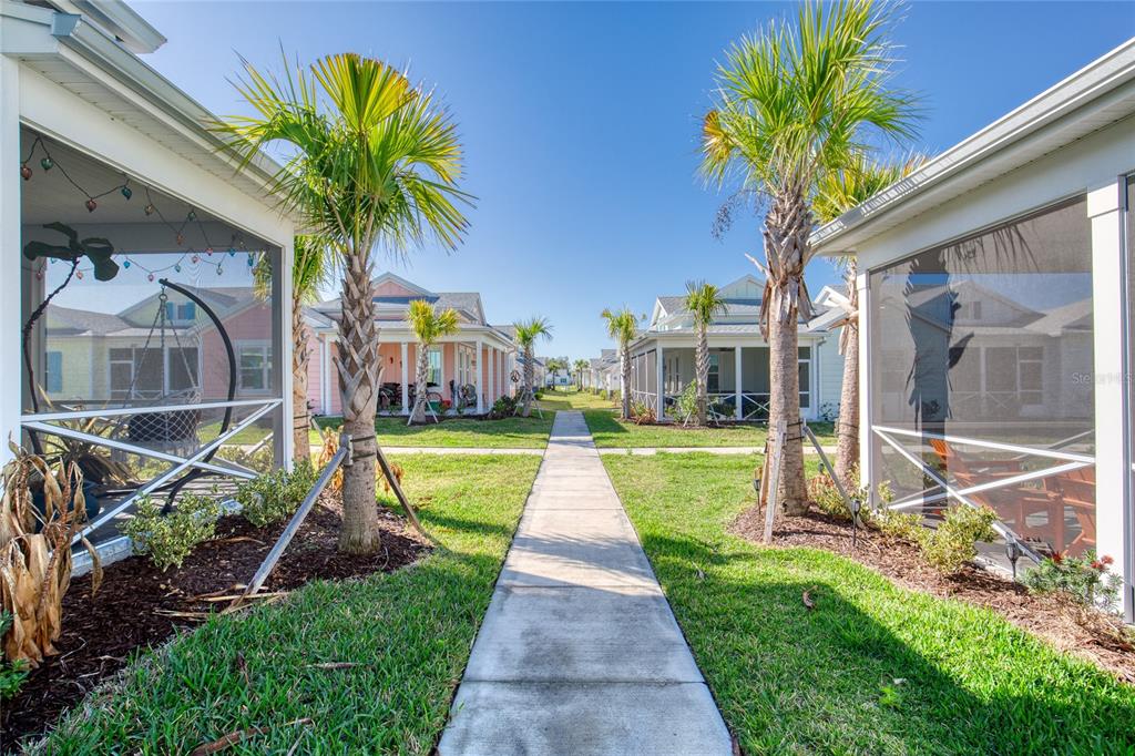 A concrete walkway leads between two screened-in porches and palm trees in a residential neighborhood — 373 HANG LOOSE WAY, DAYTONA BEACH, FL