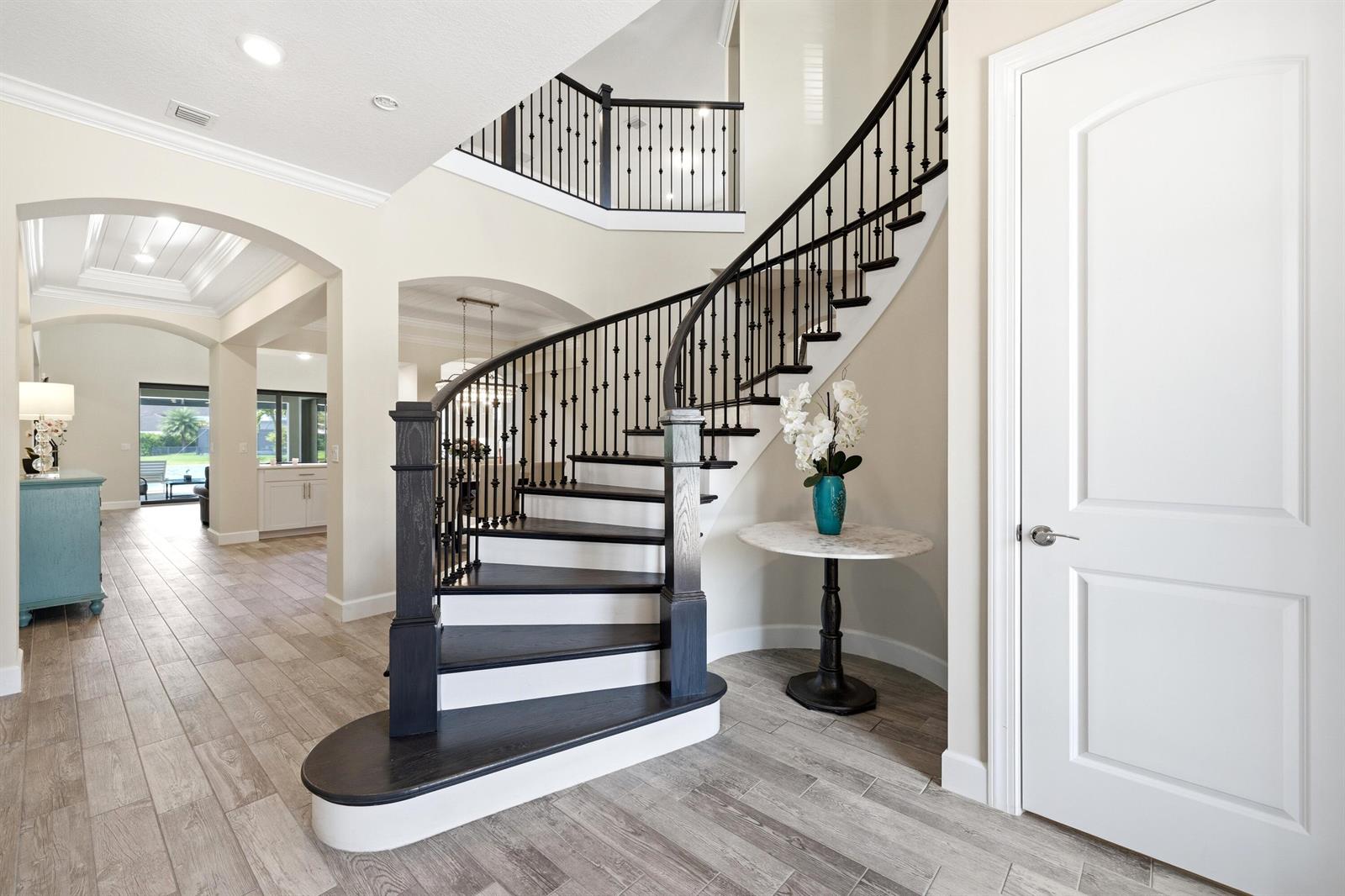 A curved staircase with dark wood treads and white risers sits in a bright foyer — 134 Indigo River Point, Jupiter FL 33478, JUPITER, FL