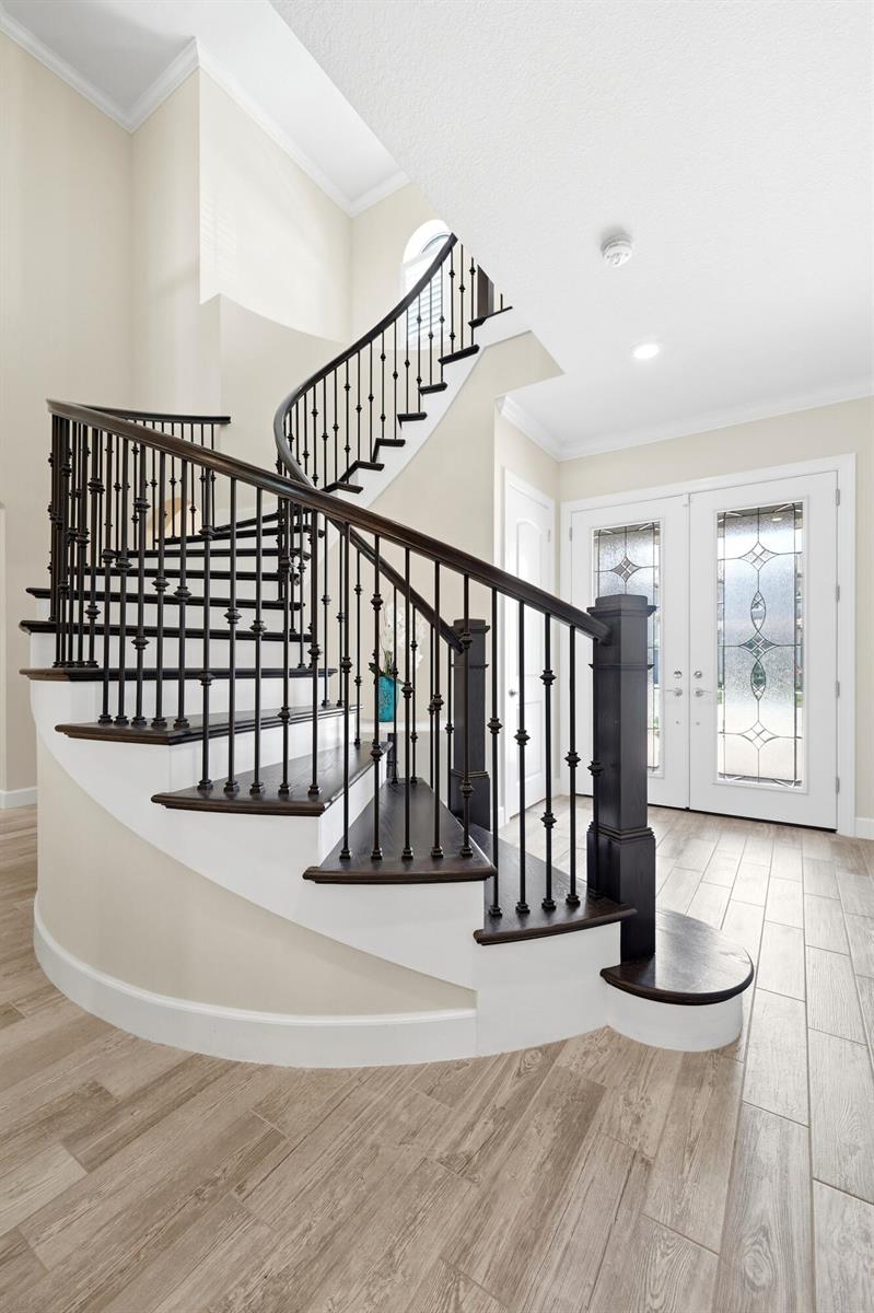 A curved staircase with dark wood treads and black metal railings stands in an entryway — 134 Indigo River Point, Jupiter FL 33478, JUPITER, FL