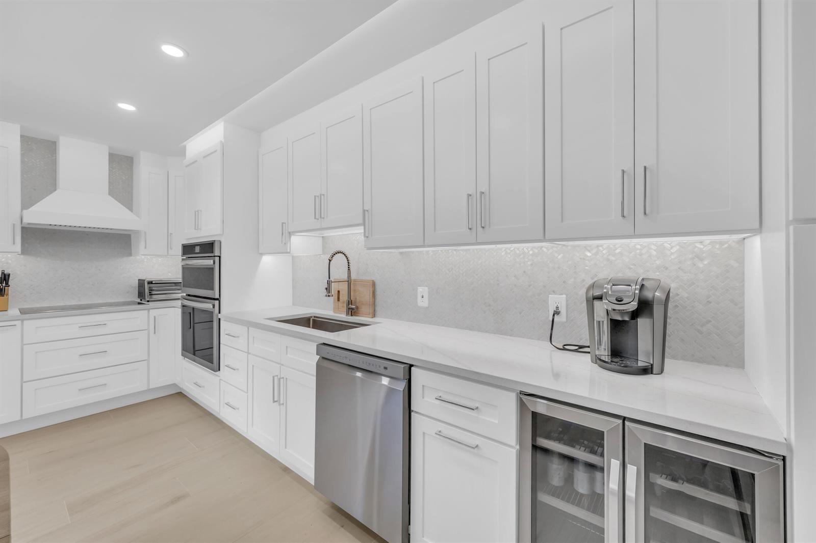 A modern white kitchen features stainless steel appliances, quartz countertops, and light wood flooring — 1208 12th Court, Jupiter FL 33477, JUPITER, FL