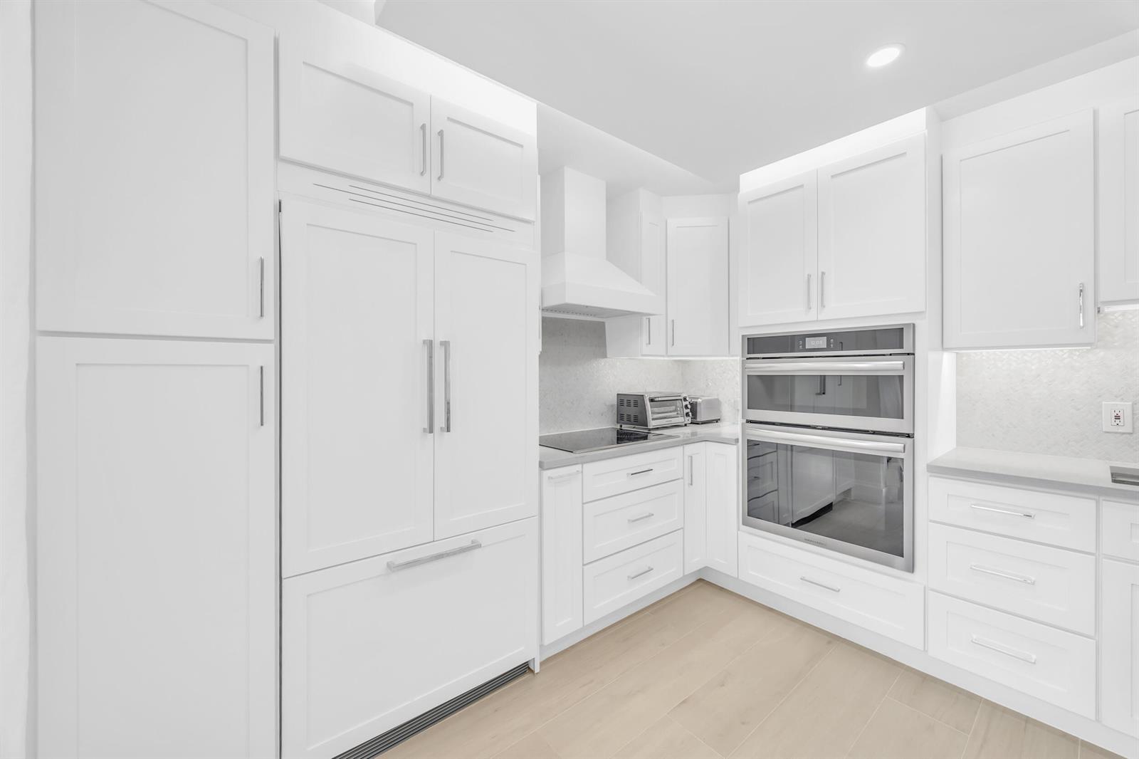 A modern white kitchen features stainless steel double wall ovens and a paneled refrigerator — 1208 12th Court, Jupiter FL 33477, JUPITER, FL