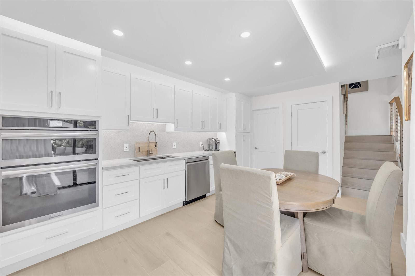 A modern white kitchen features a double wall oven, stainless steel appliances, and a dining table — 1208 12th Court, Jupiter FL 33477, JUPITER, FL