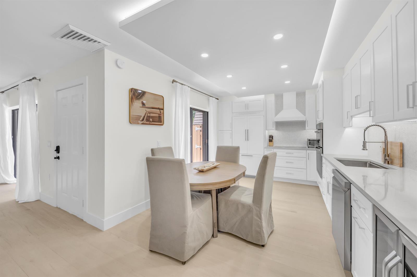 A bright, modern kitchen and dining area with white cabinetry, light wood floors, and furniture — 1208 12th Court, Jupiter FL 33477, JUPITER, FL