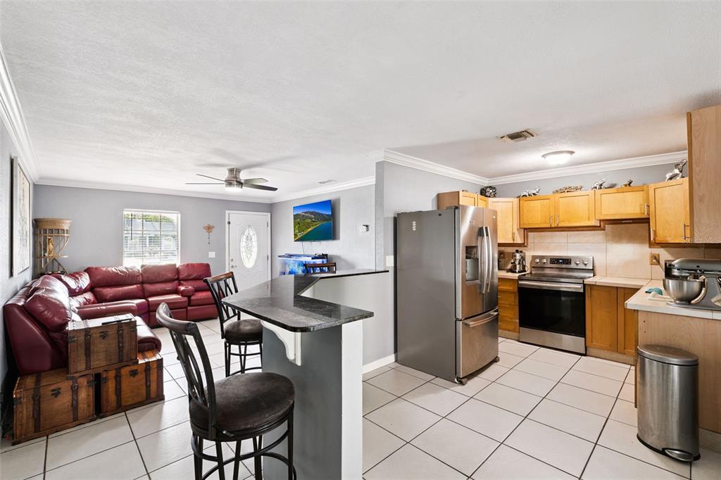 A kitchen features stainless steel appliances, light wood cabinets, and white tiled flooring — 6694 RIVO ALTO AVENUE, ORLANDO, FL