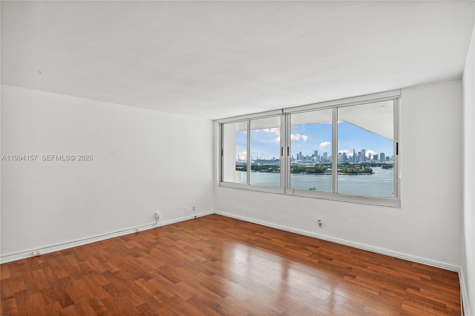 An empty room with hardwood floors and large windows overlooking a bay and city skyline — 1200 West Ave # 01, Miami Beach FL 33139, MIAMI BEACH, FL