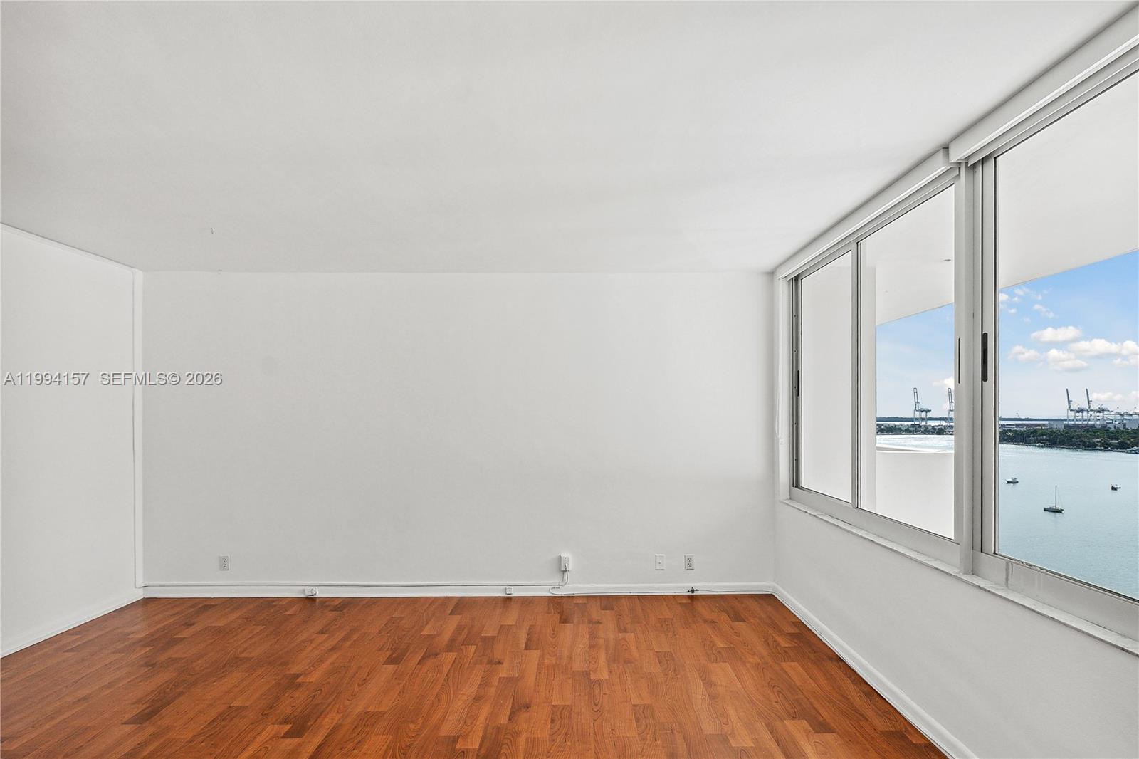 An empty room with white walls, hardwood floors, and a large window overlooking the water — 1200 West Ave # 01, Miami Beach FL 33139, MIAMI BEACH, FL