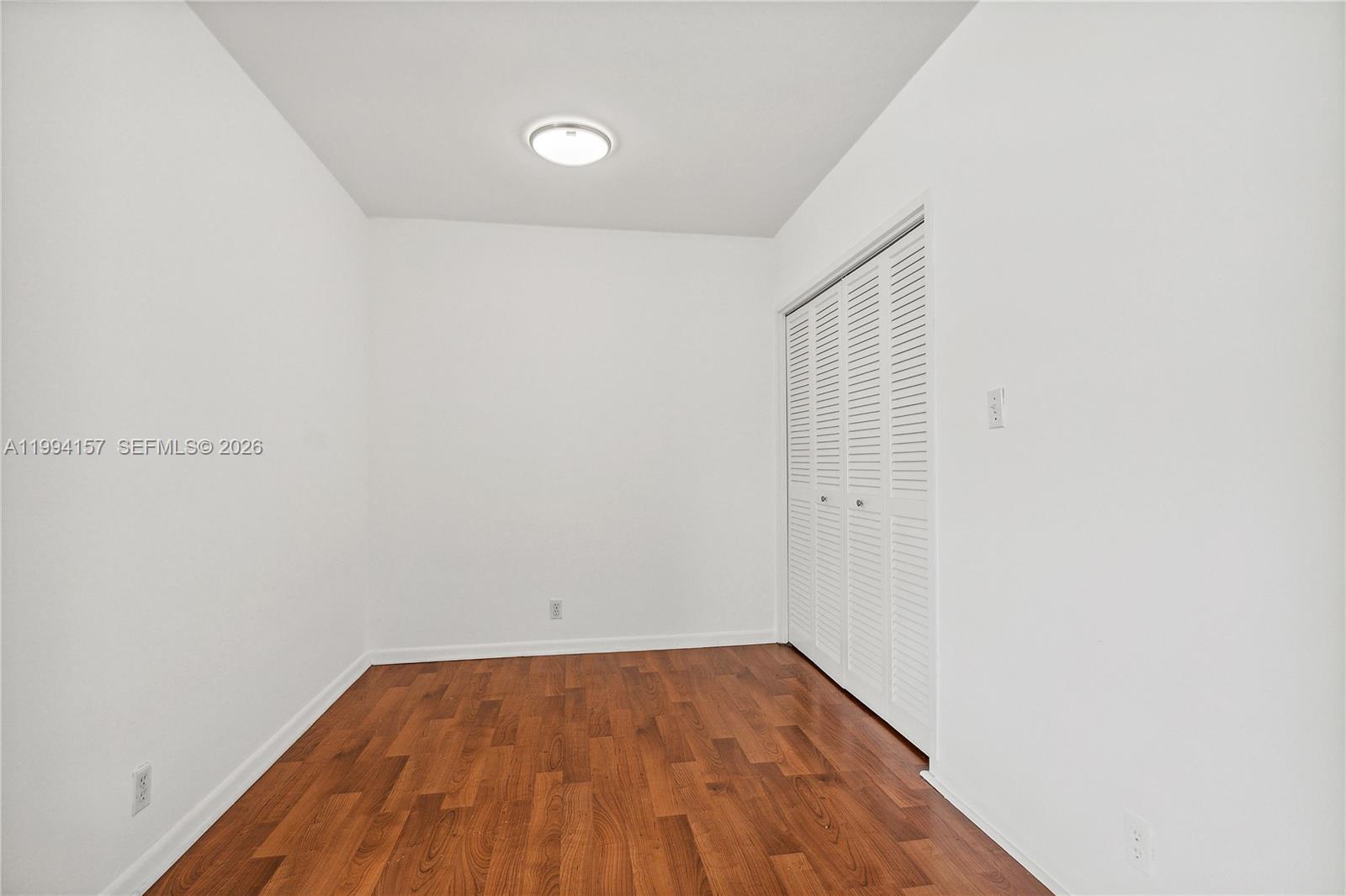 A small, empty room features white walls, wood-look flooring, a ceiling light, and louvered closet doors — 1200 West Ave # 01, Miami Beach FL 33139, MIAMI BEACH, FL