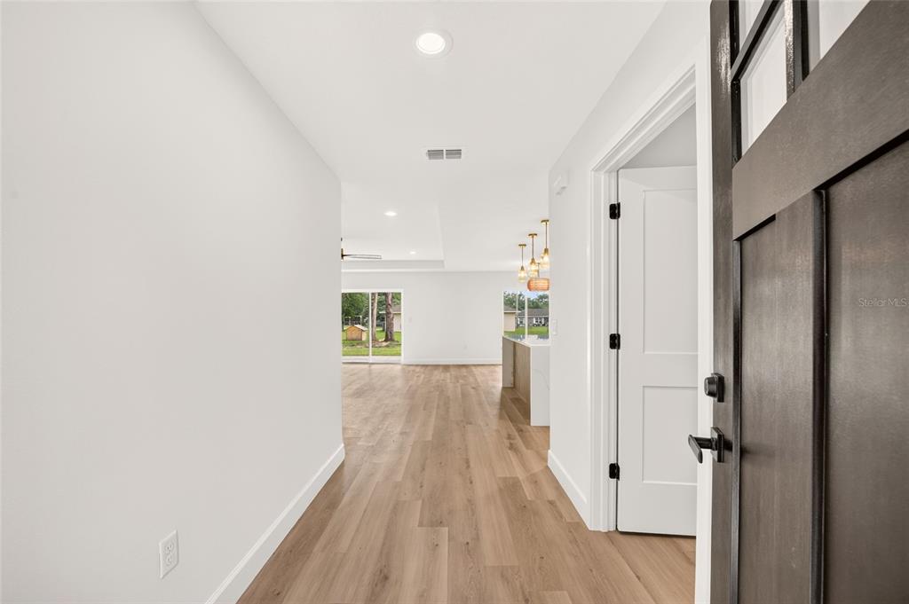A bright entryway with wood-look flooring leads into an open-concept living area and kitchen — 4252 SE 135 LANE, SUMMERFIELD, FL