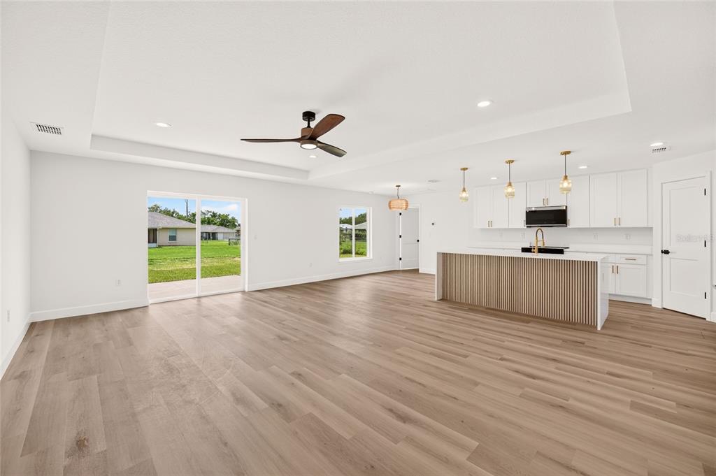 An open-concept living area with light wood floors, a kitchen island, and sliding glass doors — 4252 SE 135 LANE, SUMMERFIELD, FL