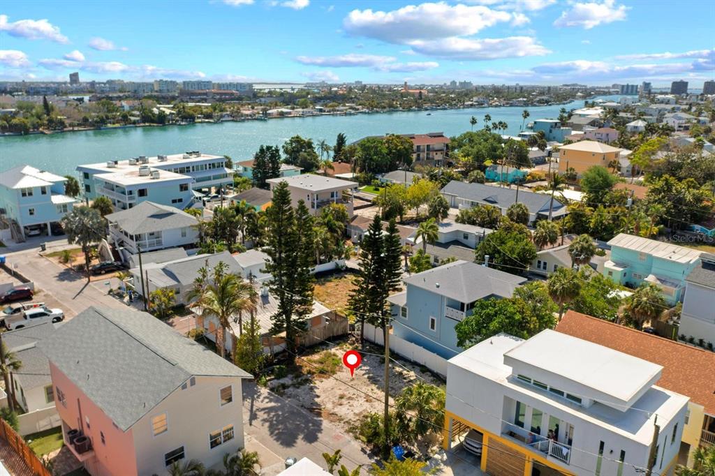 An aerial view shows a vacant residential lot situated between two houses near the water — 119 95TH AVENUE, TREASURE ISLAND, FL