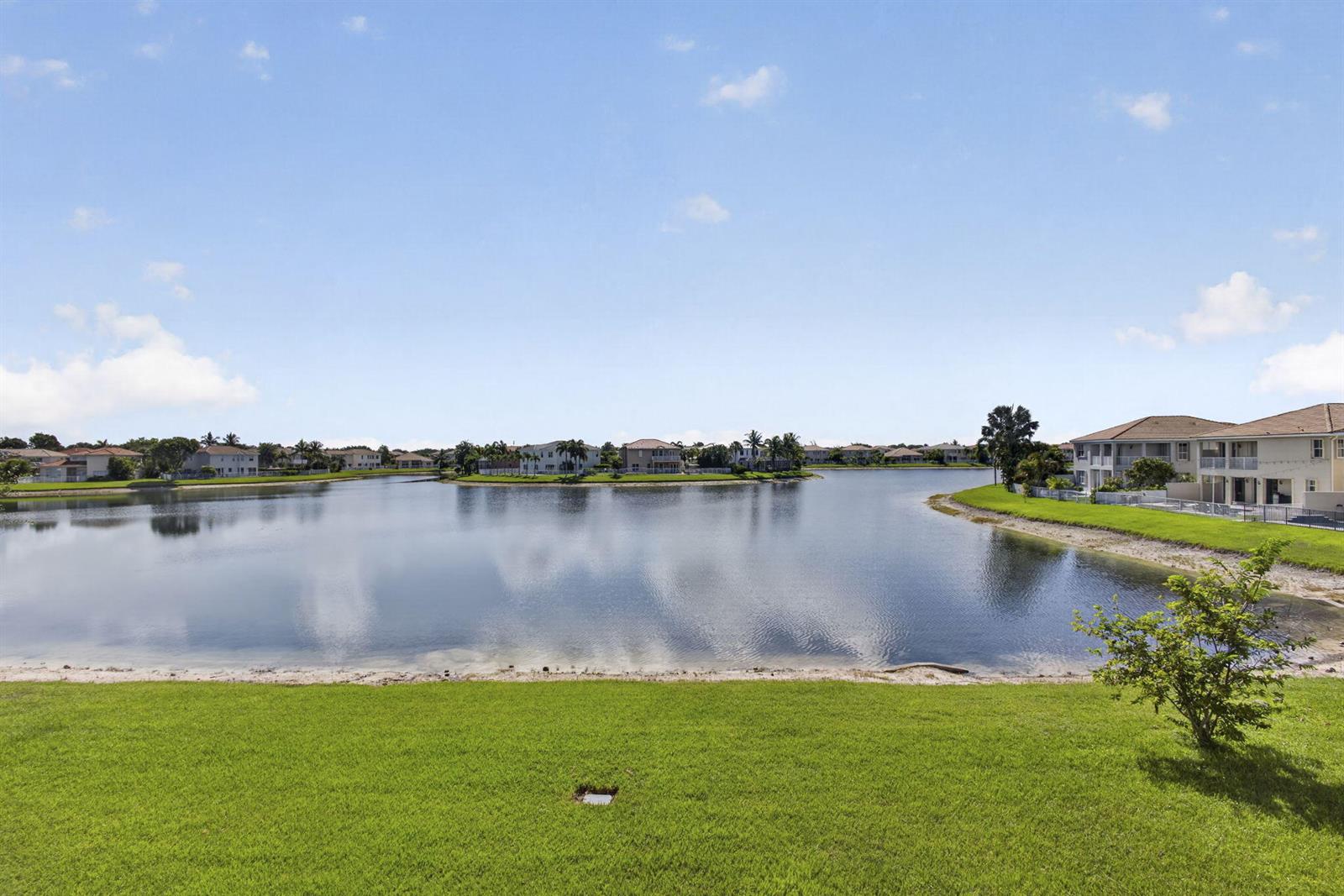 A view of a lake surrounded by residential houses and green lawns under a blue sky — 10675 Old Hammock Way, Wellington FL 33414, WELLINGTON, FL