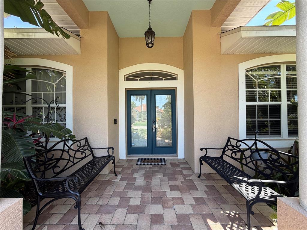 A covered entryway features a double glass door, two black metal benches, and paver flooring — 9243 13TH AVENUE CIRCLE NW, BRADENTON, FL