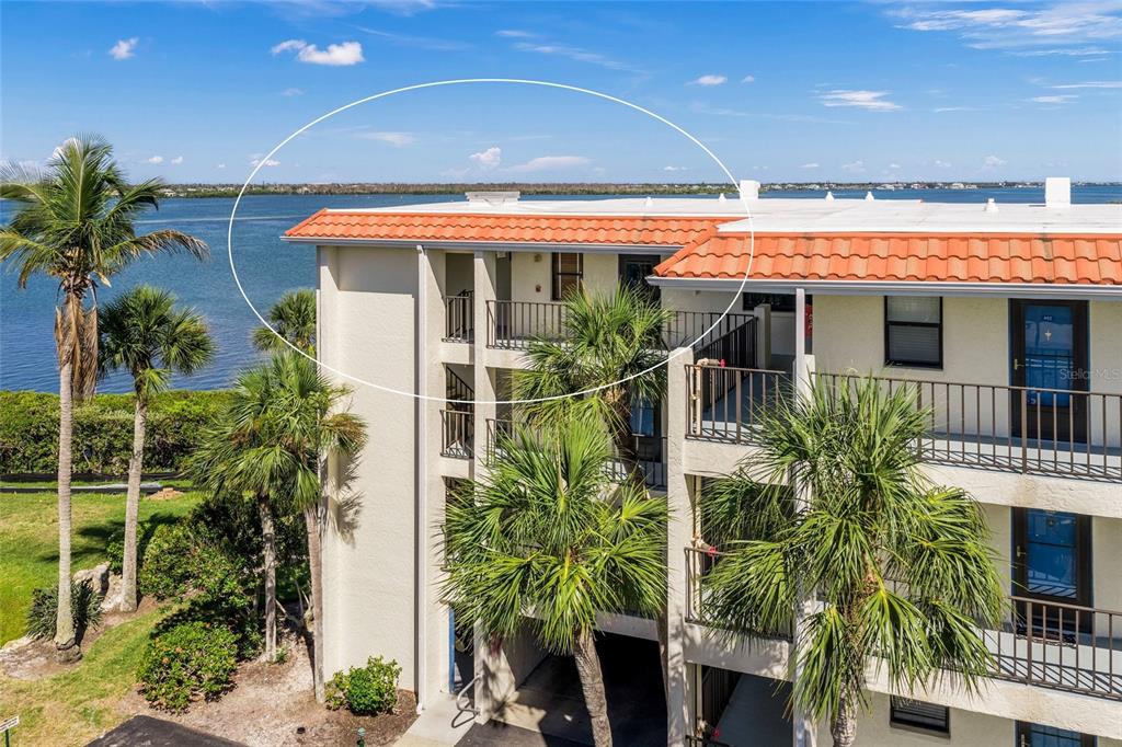 An exterior view of a multi-story apartment building with a tiled roof overlooking water — 1591 BEACH ROAD UNIT 401, ENGLEWOOD, FL