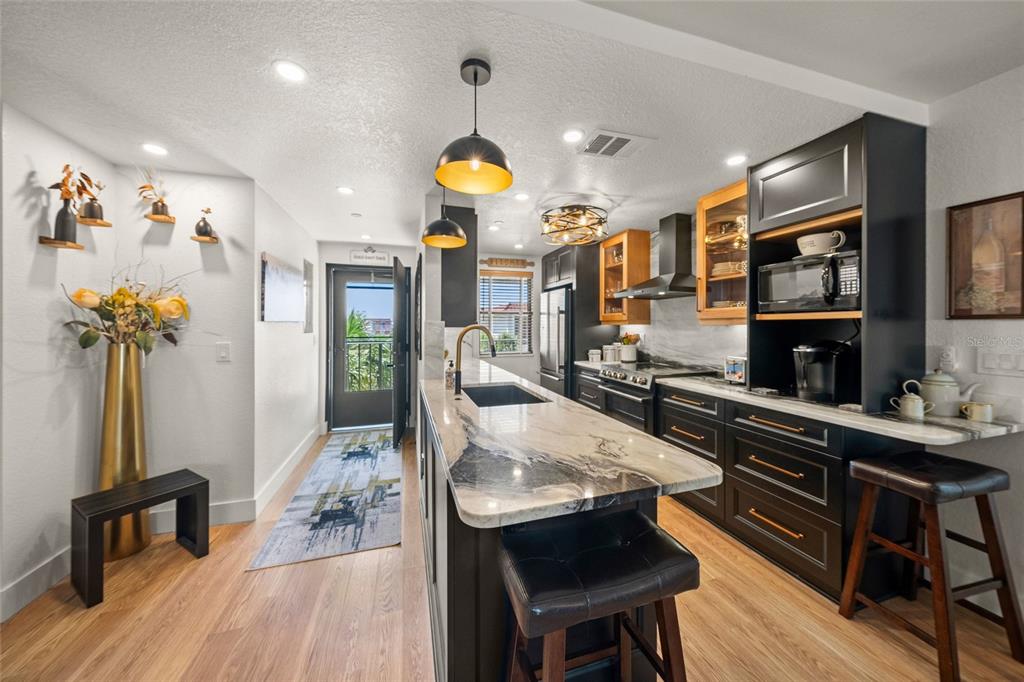 A modern kitchen features dark cabinetry, a marble-topped island, and a doorway leading to a balcony — 1591 BEACH ROAD UNIT 401, ENGLEWOOD, FL