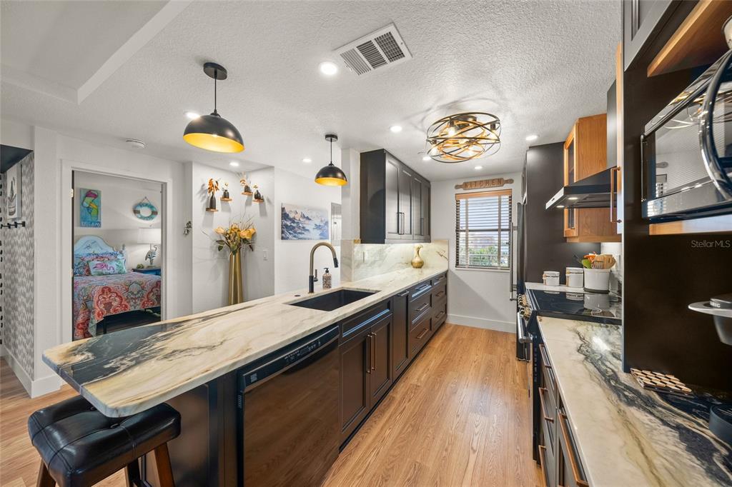 A kitchen features dark cabinetry, a long marble-patterned island, and wood-look flooring — 1591 BEACH ROAD UNIT 401, ENGLEWOOD, FL