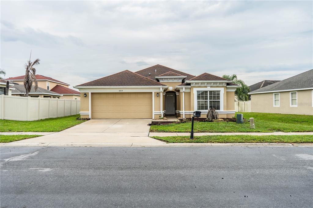 A single-story tan house with a two-car garage and a brown shingled roof — 6015 CHAMPLAIN PASS, LAKELAND, FL