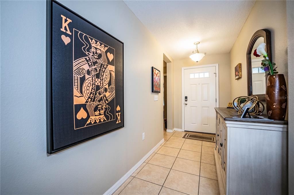 An entryway features tile flooring, a large King of Hearts wall art, and a wooden console — 6015 CHAMPLAIN PASS, LAKELAND, FL