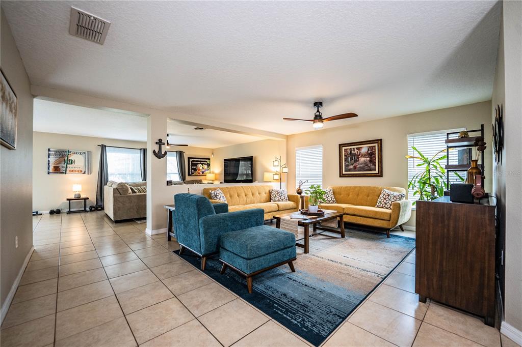 A living room features yellow sofas, a blue armchair with ottoman, and tile flooring — 6015 CHAMPLAIN PASS, LAKELAND, FL
