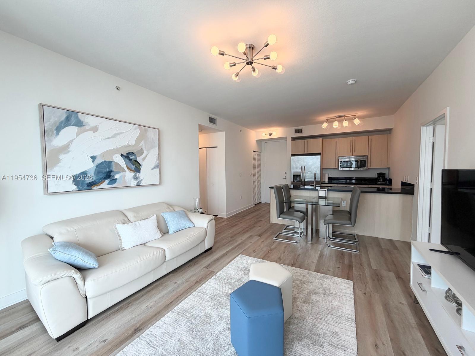 This living room features light wood flooring, a white sofa, and an open kitchen area — 1111 SW 1 AV, Miami FL 33130, MIAMI, FL