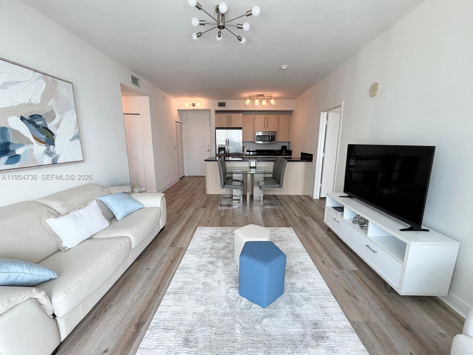 A living room with light wood flooring, a white sofa, and an open kitchen area — 1111 SW 1 AV, Miami FL 33130, MIAMI, FL