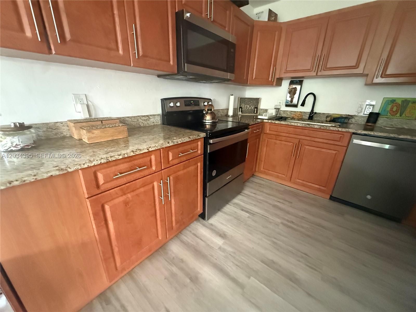A kitchen features wood cabinets, granite countertops, stainless steel appliances, and light-colored wood flooring — 2538 Coolidge St, Hollywood FL 33020, HOLLYWOOD, FL